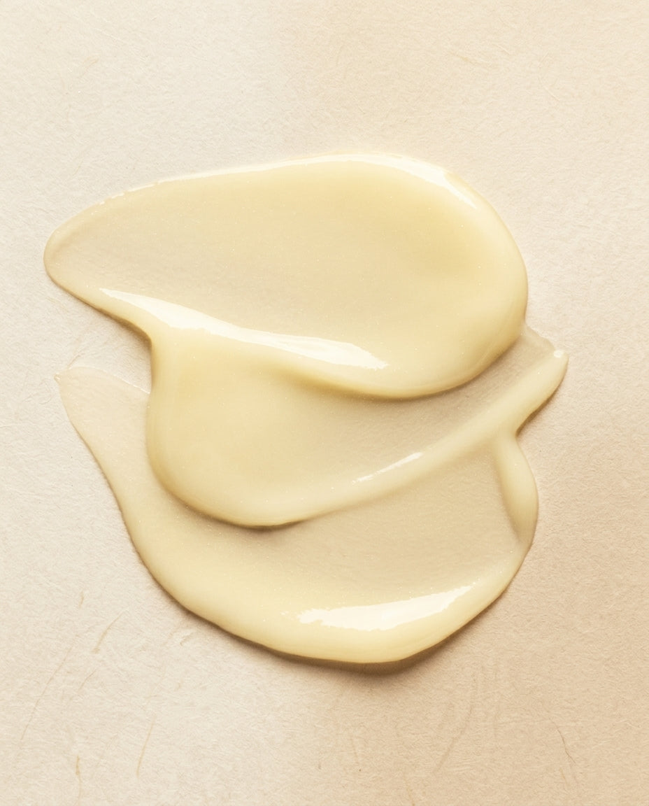 A dollop of creamy, pale yellow cosmetic cream or foundation swirled on a textured beige surface.